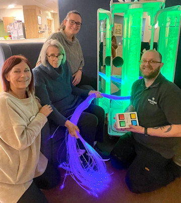 Asset - Belong Crewe resident, Sheila Manning (seated) tries out the new Namaste machine 
(L-R) Sharon Bull (practice development facilitator), Sheila Manning (resident), Jane Hughes (village nurse manager) and David Bithell (caretaker)