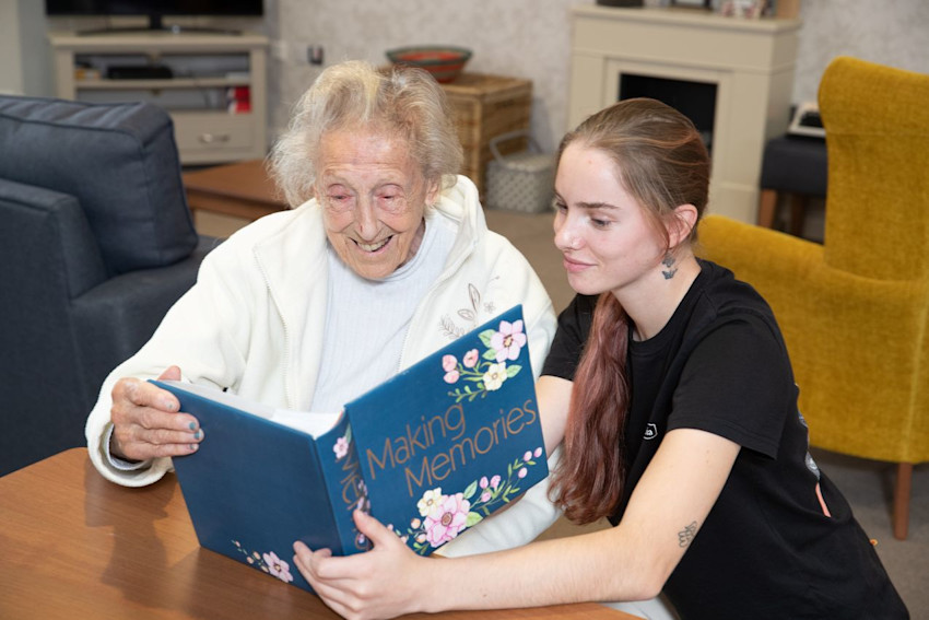Belong Chester - Carer and resident reading a book on a household